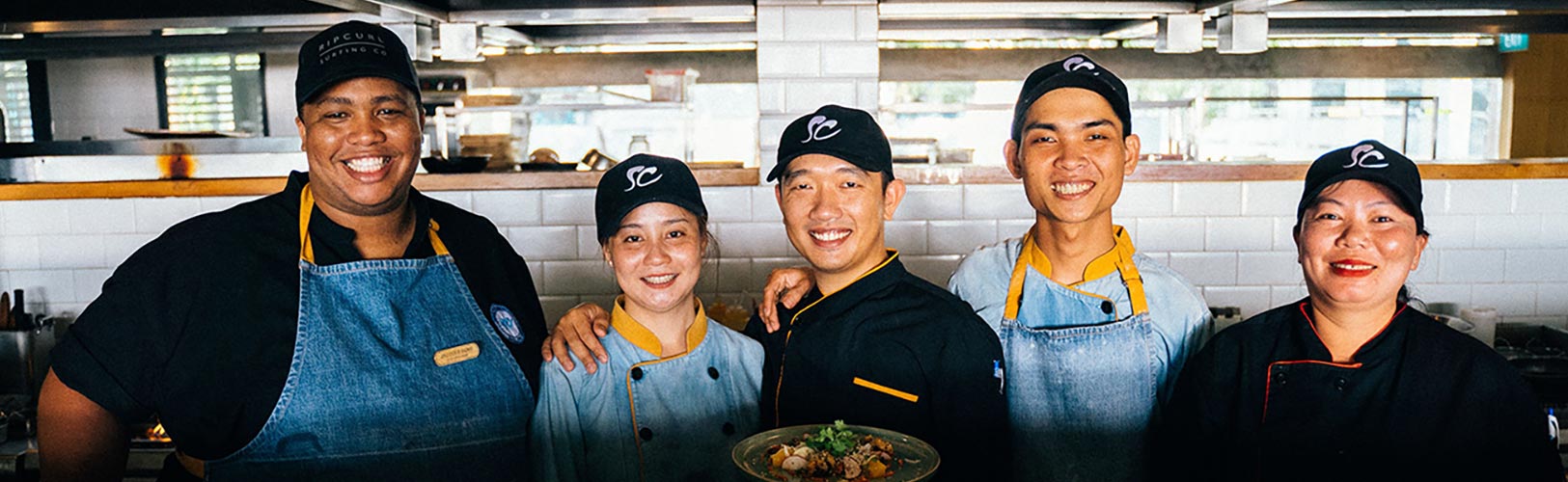 Team of restaurant employees standing side-by-side, smiling, and presenting a dish